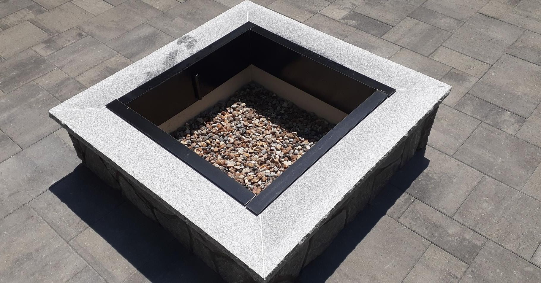 A square fire pit sitting on top of a brick patio.