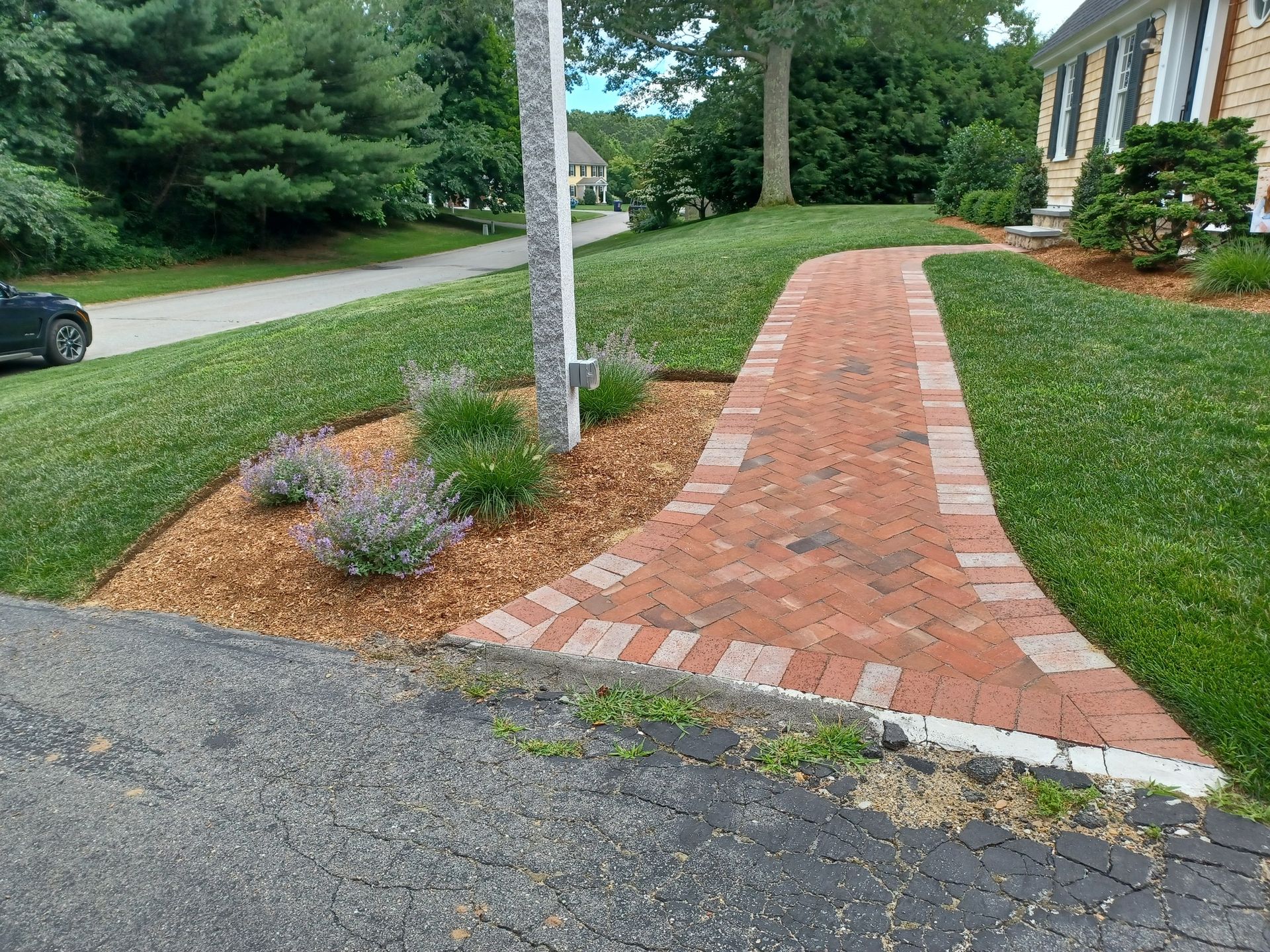 A brick walkway leading to a house with a car parked on the side of the road.