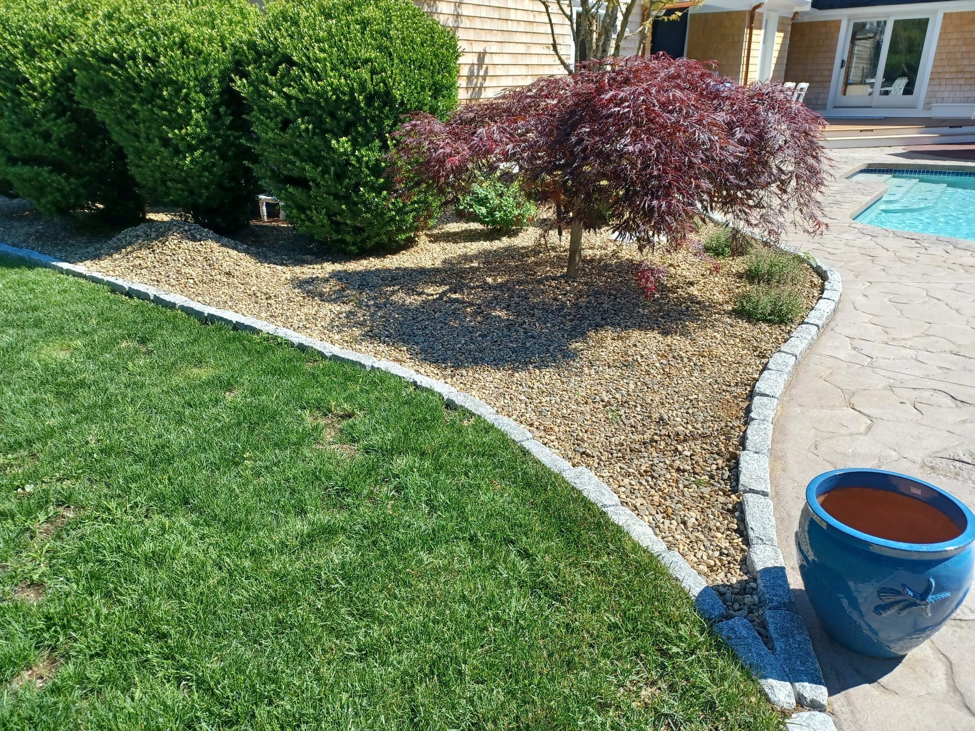 A blue pot is sitting in the middle of a lush green lawn next to a swimming pool.
