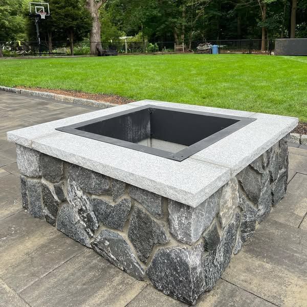 A stone fire pit is sitting on a patio next to a basketball hoop.