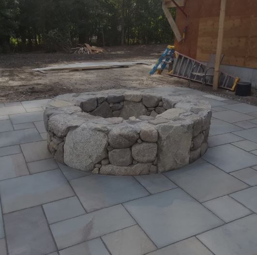 A stone fire pit is sitting on a patio next to a ladder.
