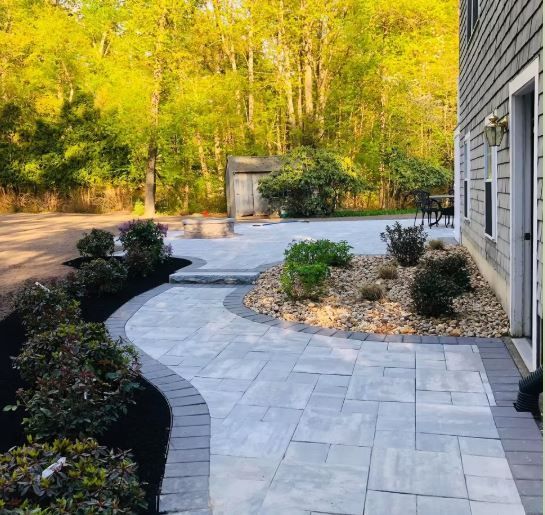 A walkway leading to a patio in front of a house surrounded by trees.