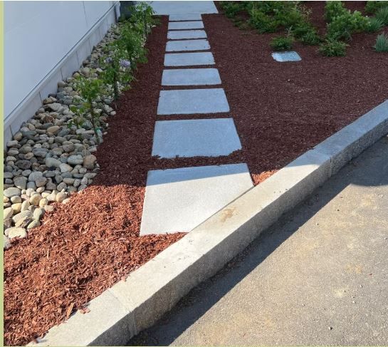 A stone walkway leading to a garden with rocks and mulch