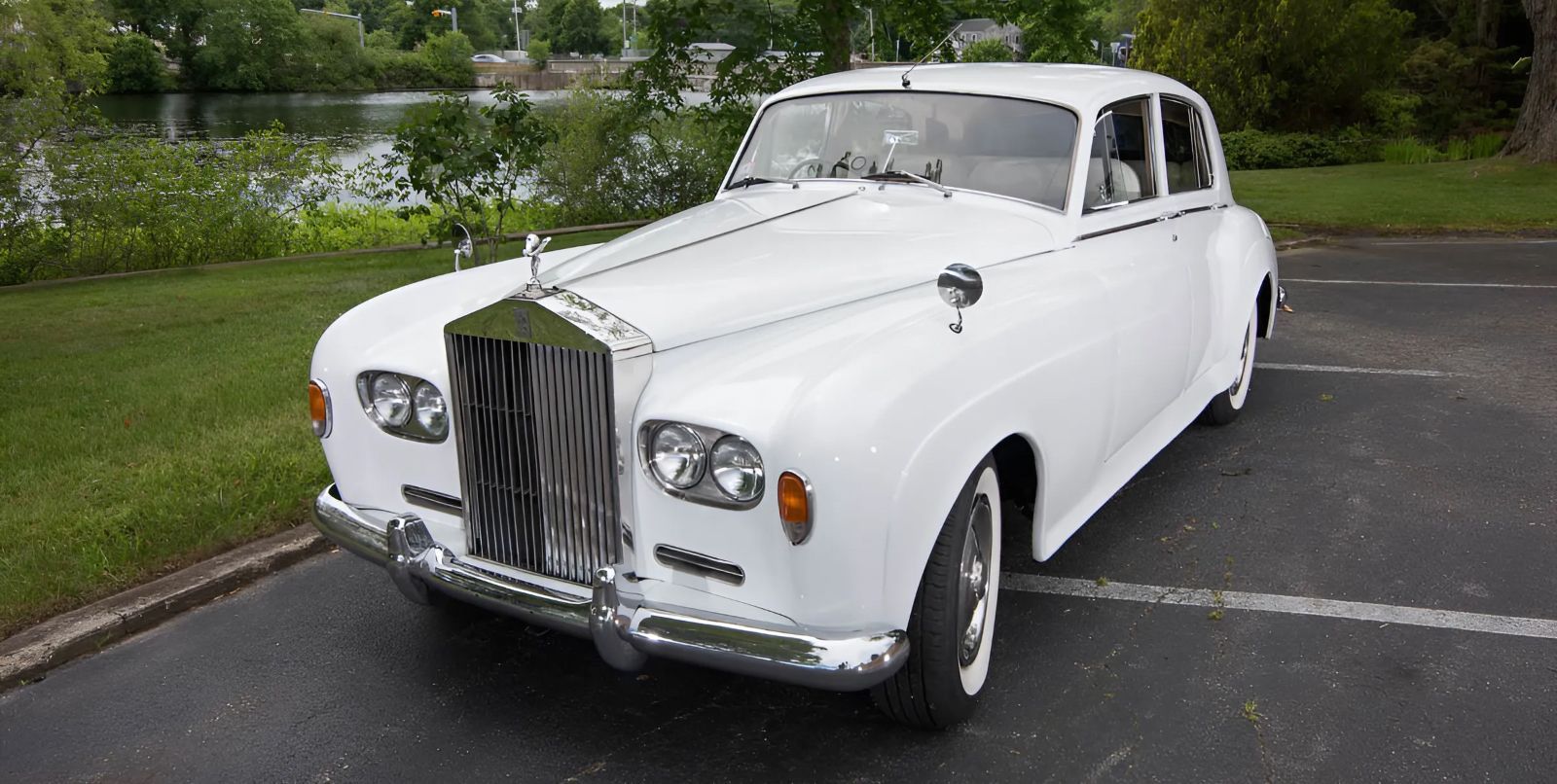 White Rolls-Royce sedan parked on asphalt near a grassy area and body of water.