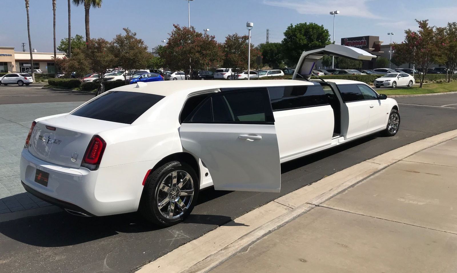 White limousine with open doors parked on a sunny day.