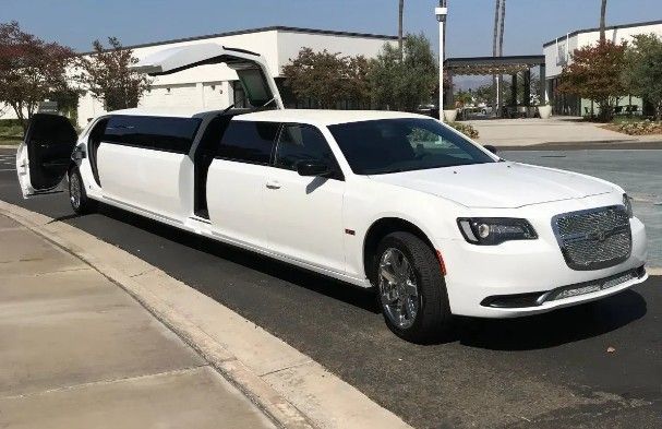 White limousine parked on a paved road, doors open. Modern building in the background.