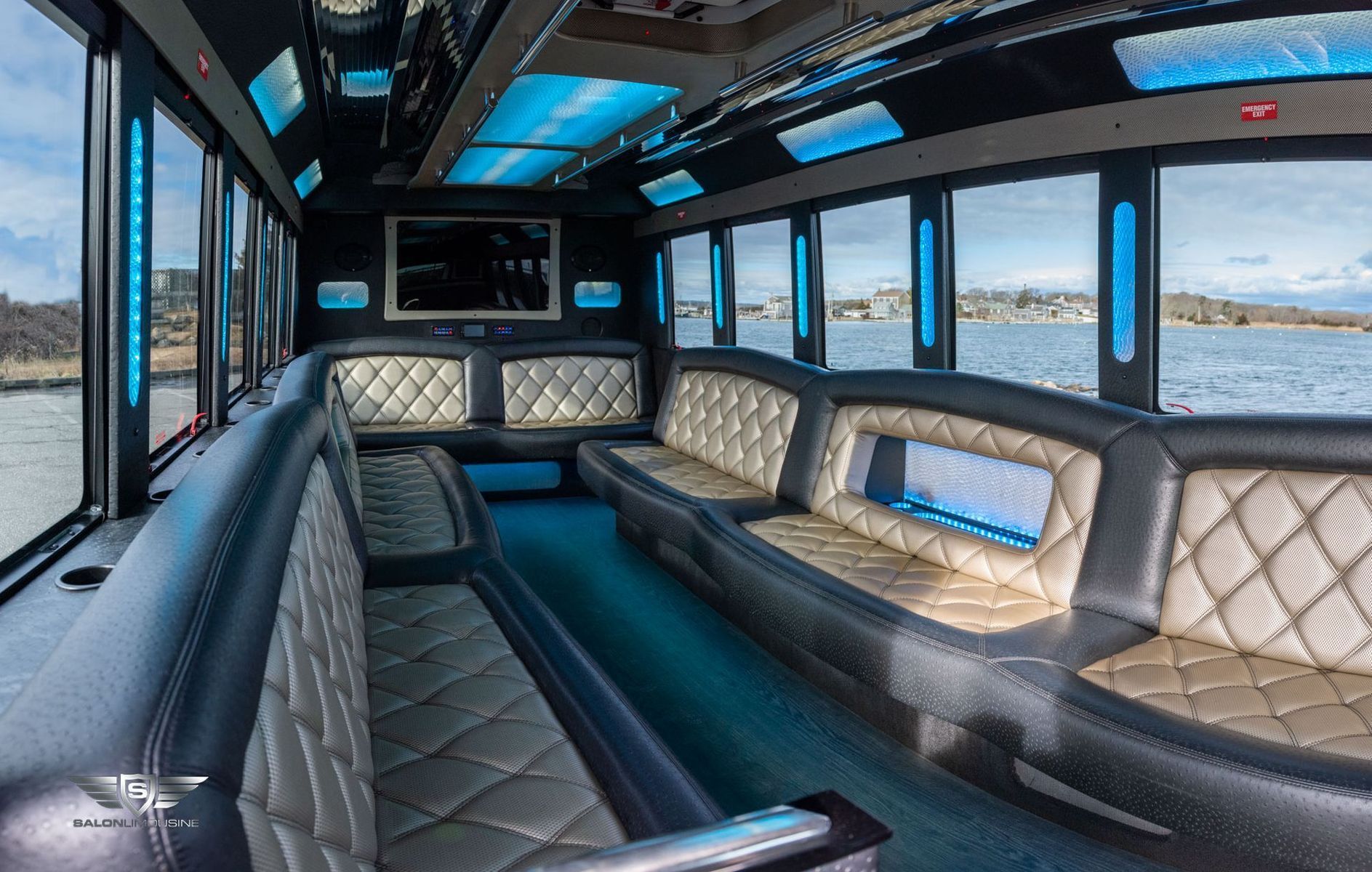 Interior of a luxury party bus with diamond-stitched seating, blue lighting, and large windows with an outdoor view.