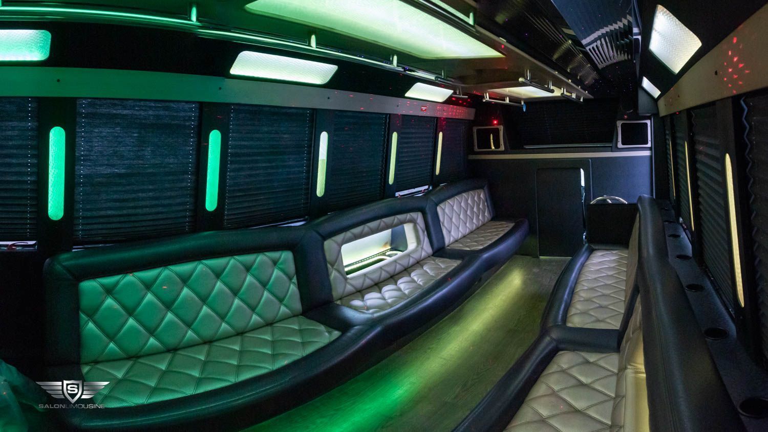 Interior of a party bus with black and green leather seating, neon green lights, and a bar area.