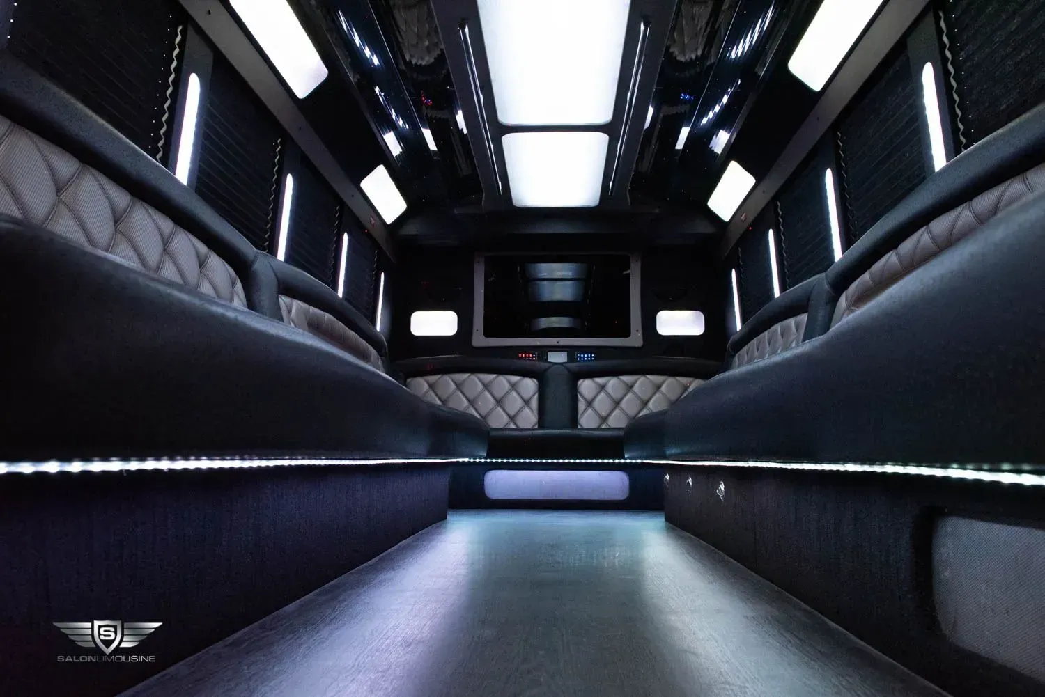 Interior of a luxury black limo van with seating, a TV, and mood lighting.