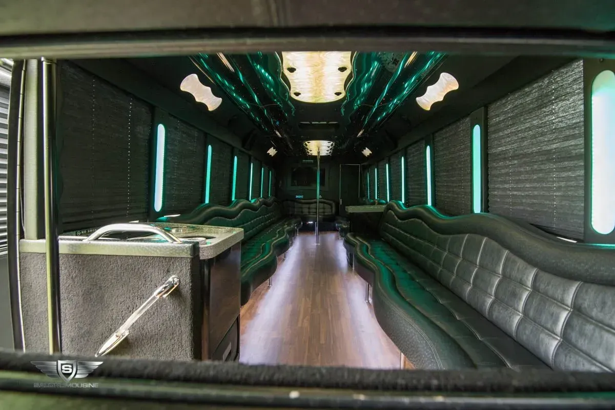 Interior of a black limousine with long seating along the sides, wooden floor, and overhead green lights.