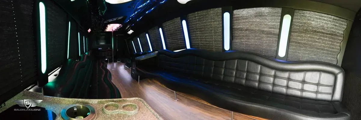 Interior of a limousine, black leather seating, reflective lighting, and a bar.