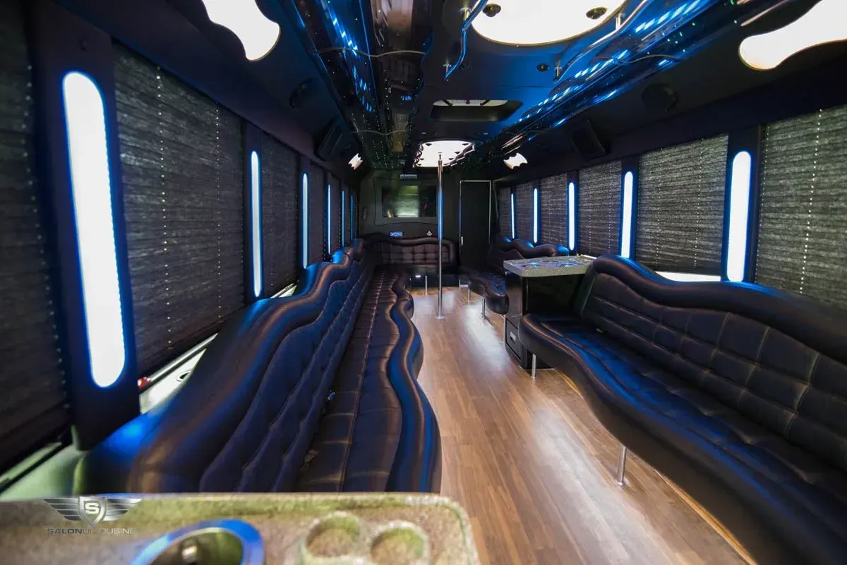 Interior of a black limousine-style party bus with blue lighting, dark leather seating, and wood flooring.