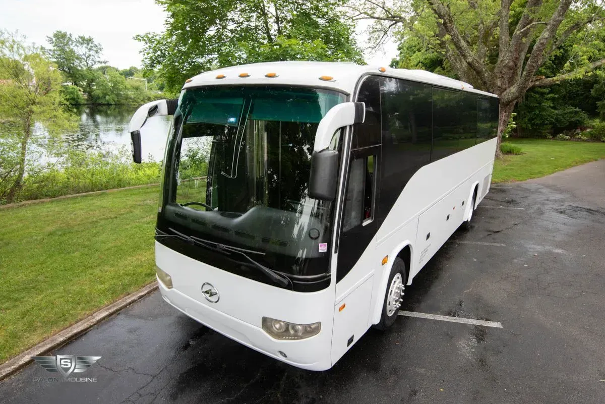White passenger bus parked on a paved area next to a green lawn and body of water.