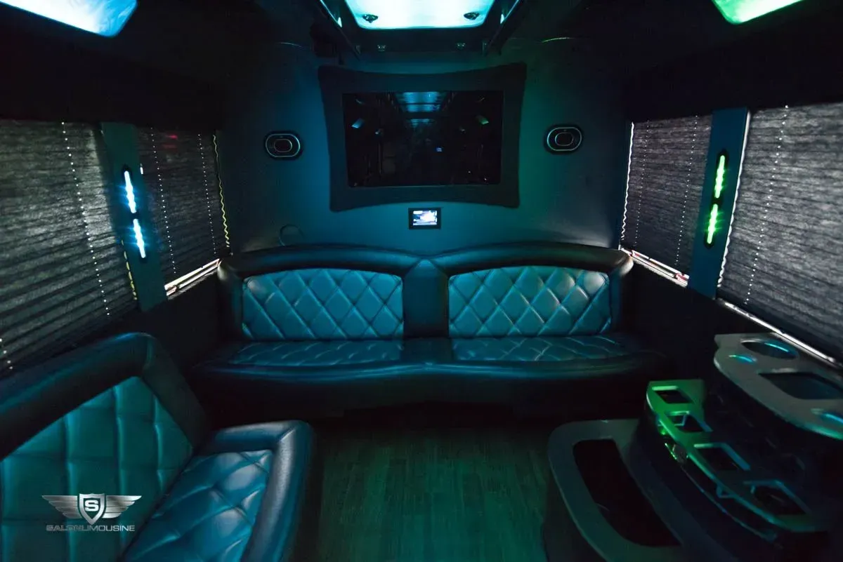Interior of a limousine with teal and black quilted leather seating, ambient lighting, and a large television.