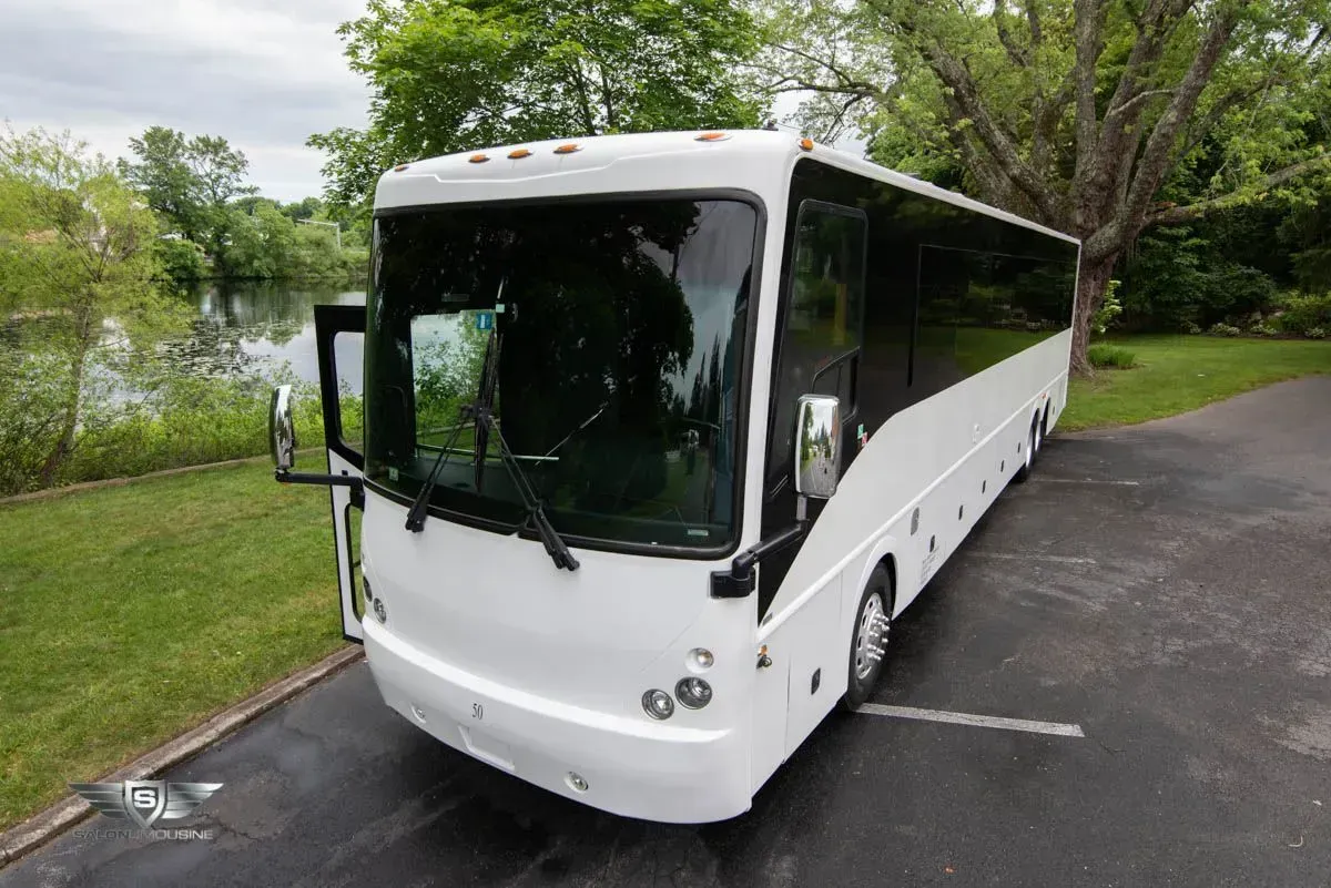 White charter bus parked on a driveway near a lake and trees.