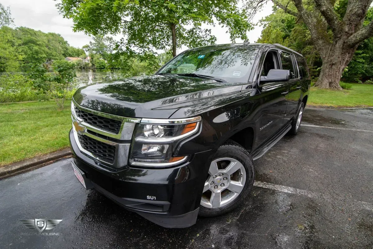 Black Chevrolet Tahoe SUV parked on wet pavement near a tree and a body of water.
