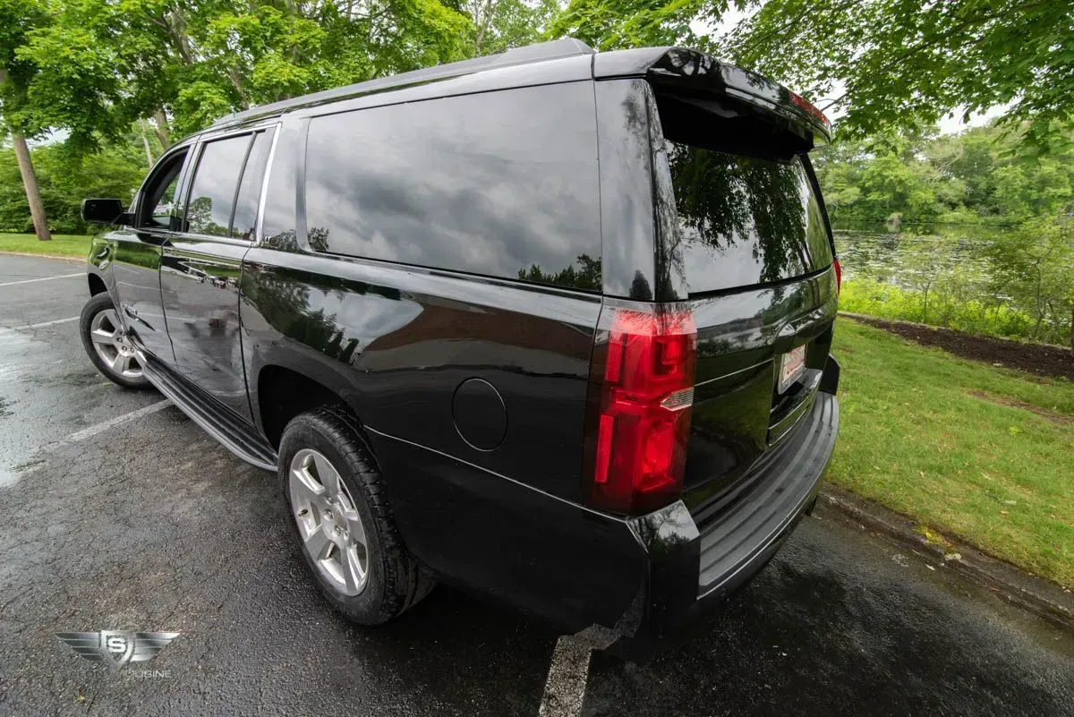Black SUV parked on asphalt next to grass and trees; rear view.