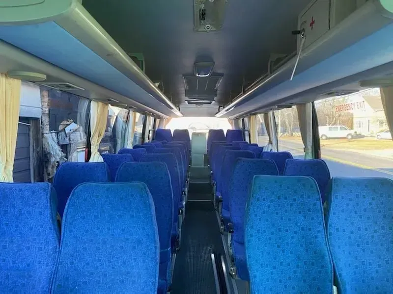 Interior of a blue bus with rows of blue seats, overhead storage, and windows along both sides.