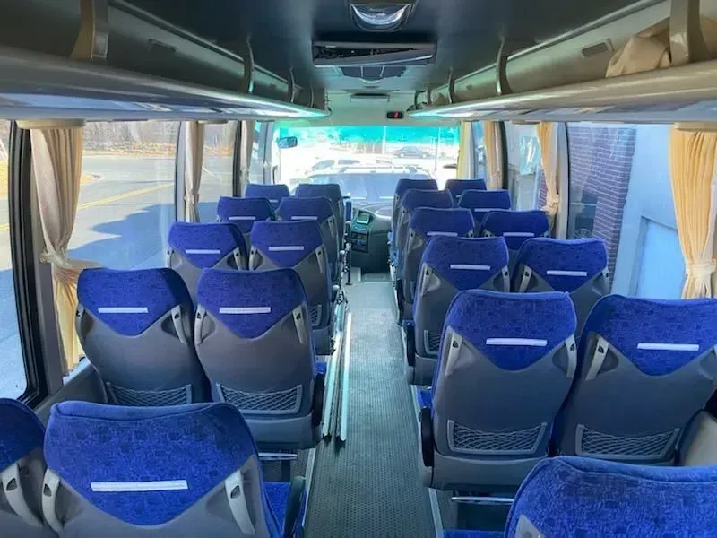 Interior view of a bus with rows of blue seats, beige curtains, and a driver's area at the front.