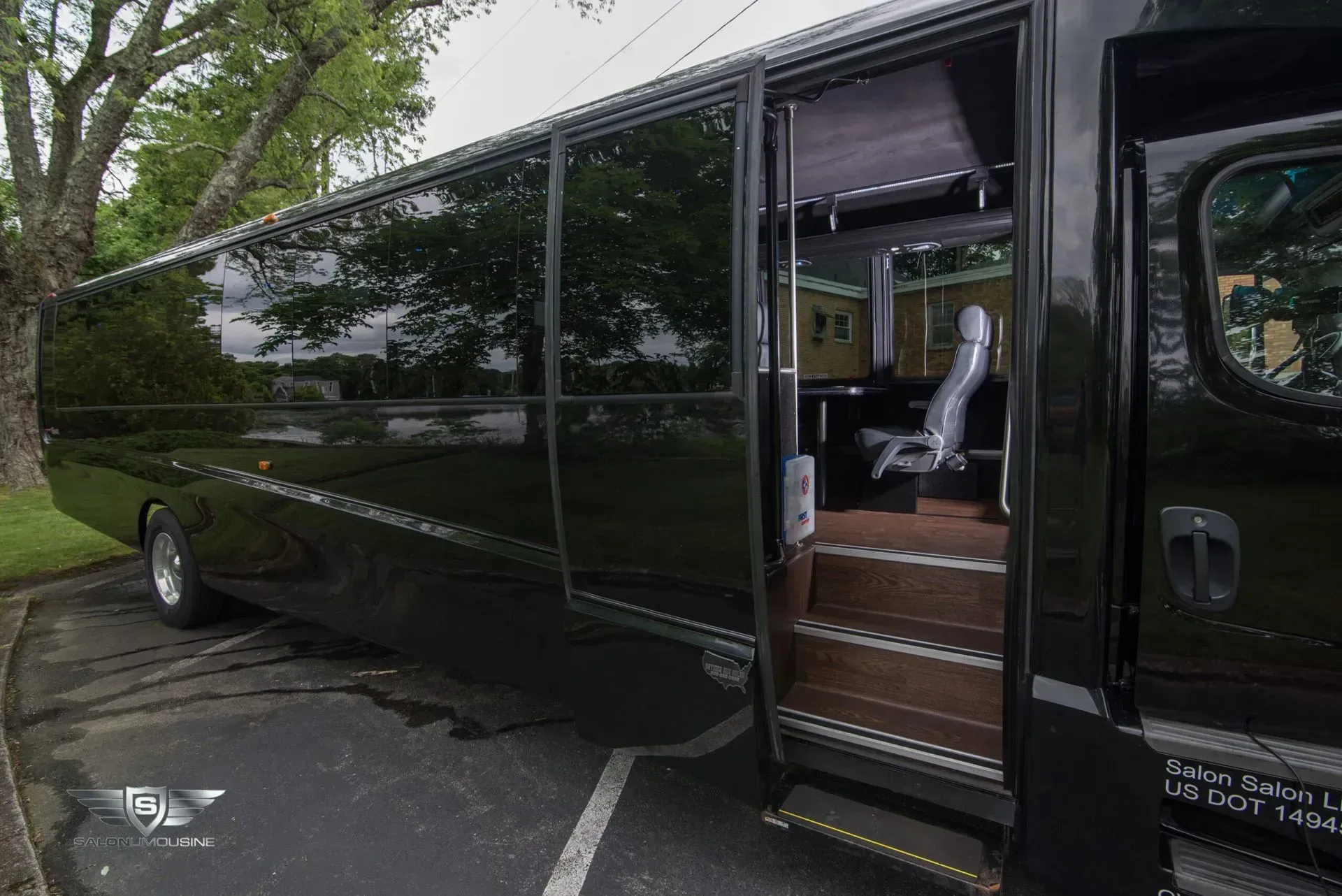 Black bus with open door, parked on pavement, revealing interior seating and steps.