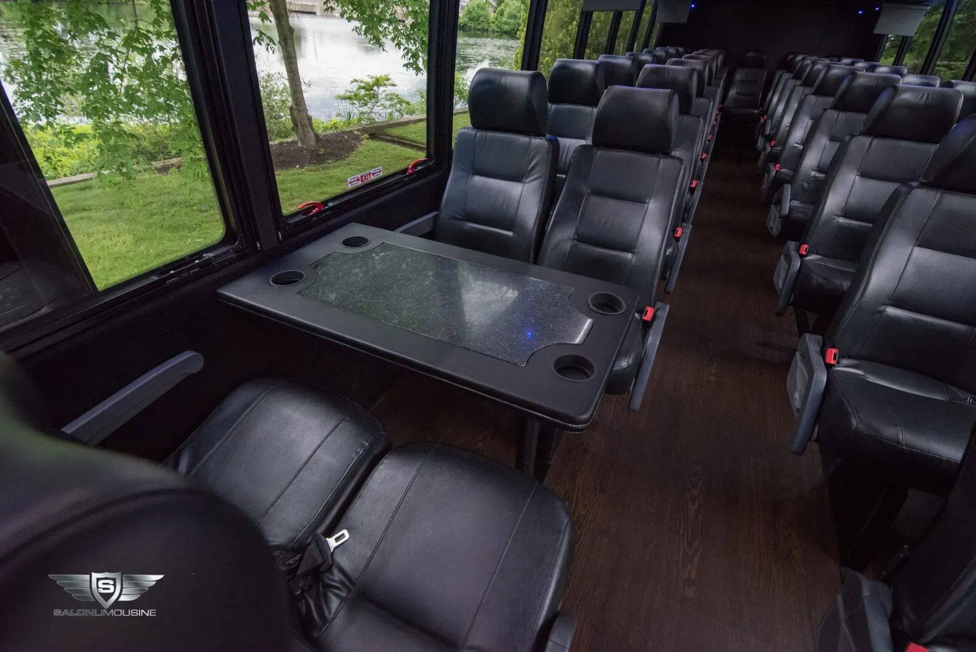 Interior view of a luxury bus with black leather seats, a table, and large windows overlooking a green landscape.