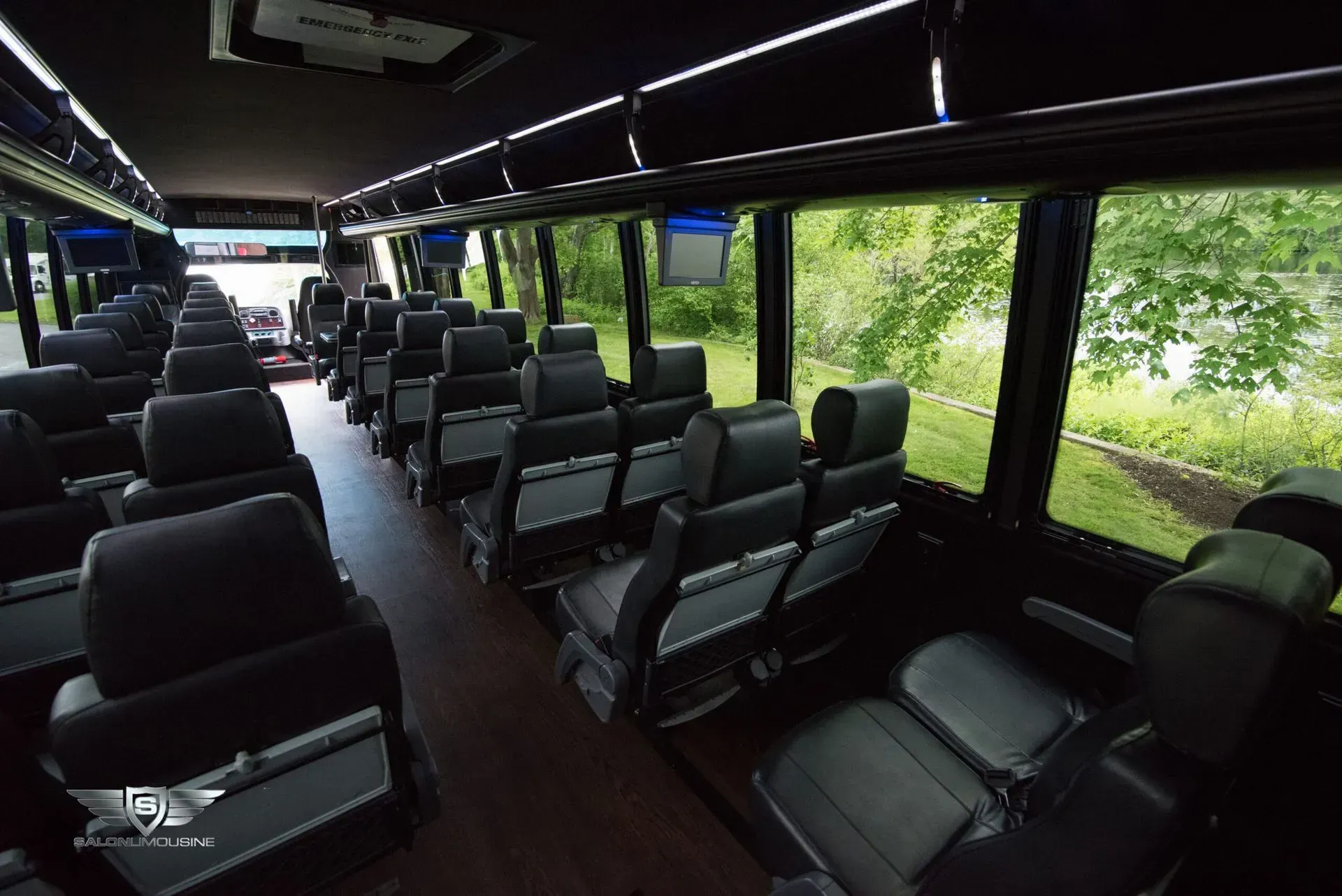 Interior of a bus, black seats in rows, large windows with a view of trees.