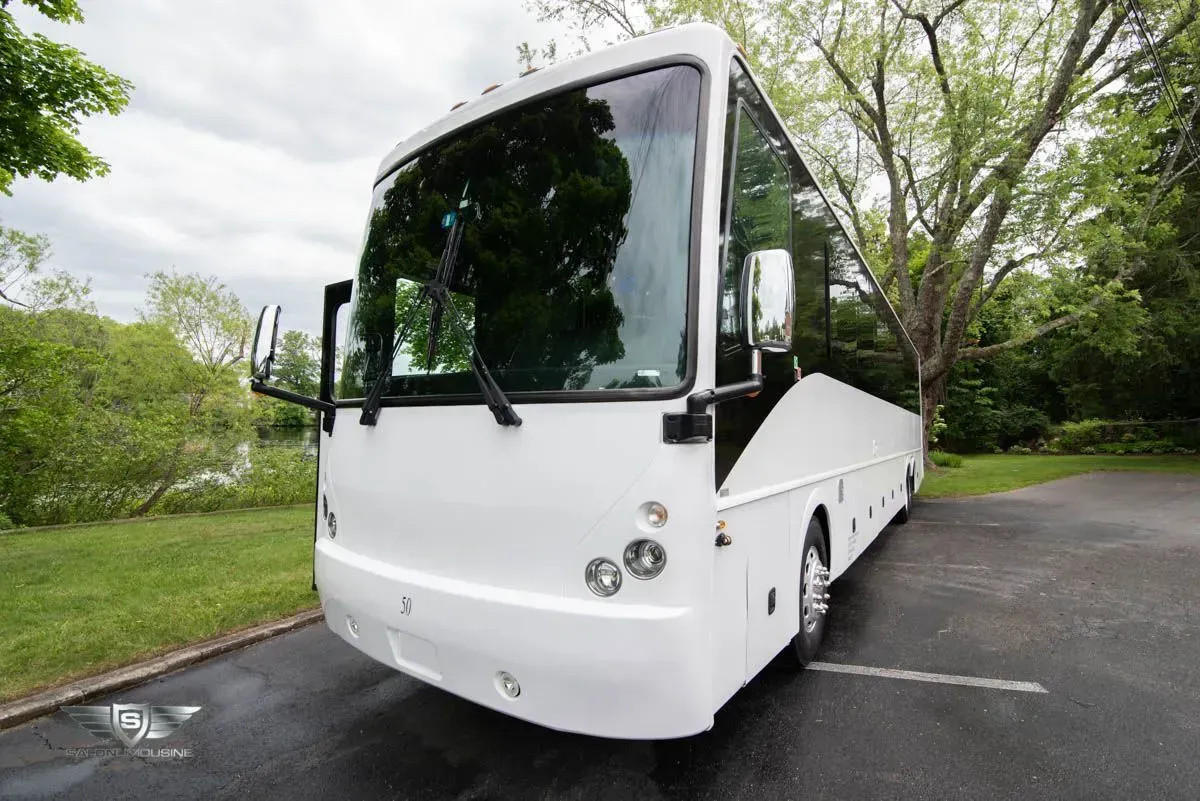 White charter bus parked on a paved driveway with greenery in the background.