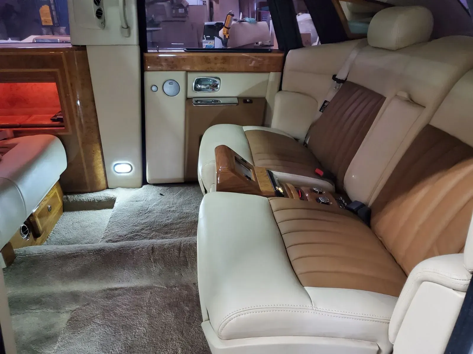 Interior of a luxury car with cream and brown leather seats, wood paneling, and plush carpet.