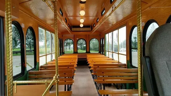 Interior of a wooden trolley with rows of benches and large arched windows. Gold accents and overhead lights.
