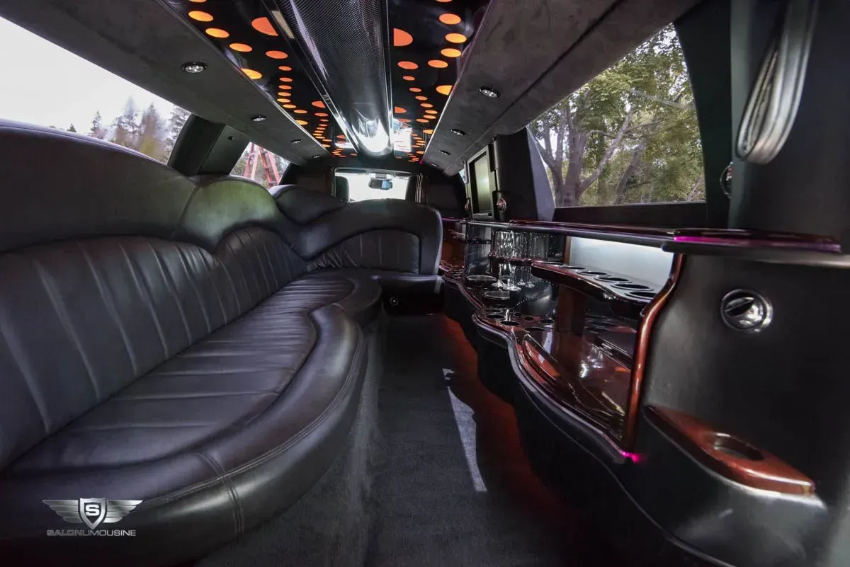 Interior of a black limousine with leather seating, mirrored bar, and starry ceiling lights.