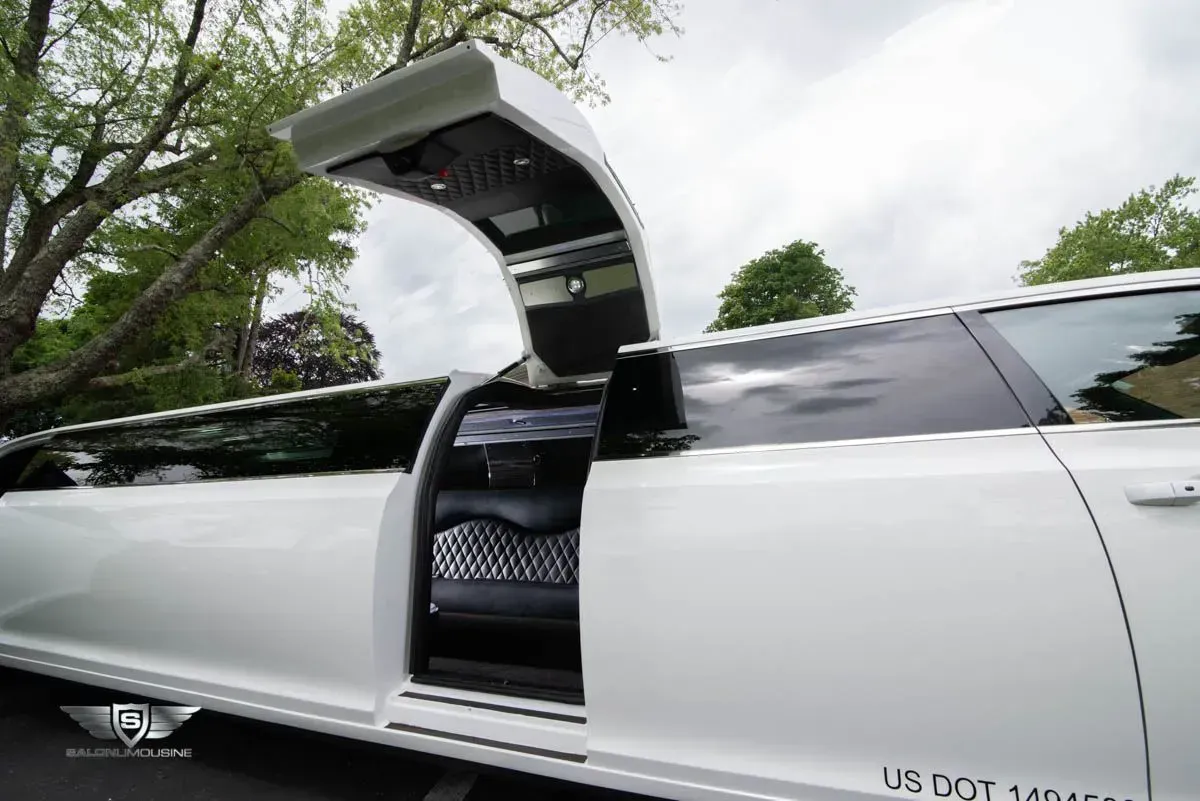 White limousine with gullwing door open, parked outdoors.