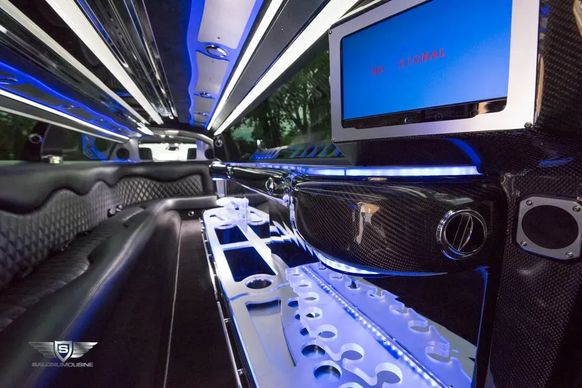 Interior of a black limousine with blue and white lighting, a TV, and seating.