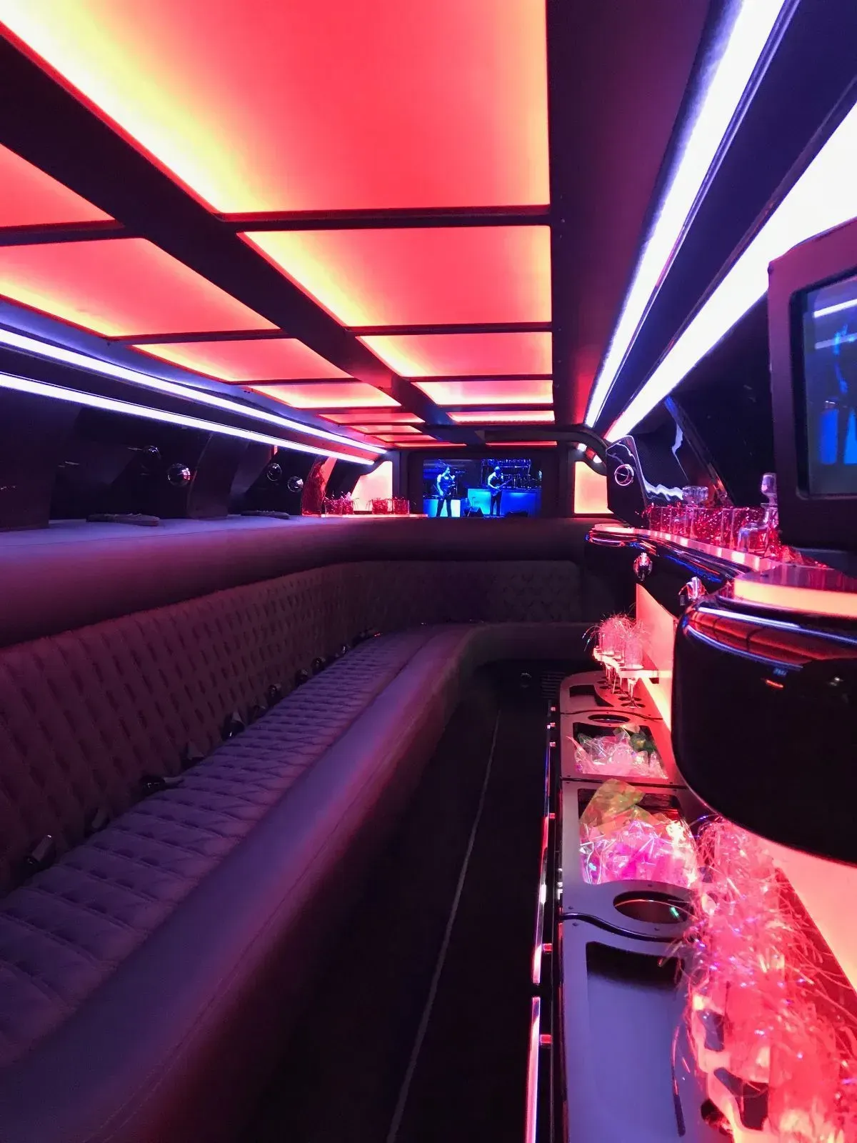 Interior of a limousine with red and purple LED lighting, leather seating, and a bar area.