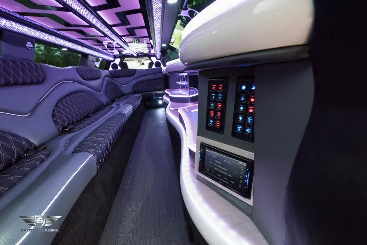 Interior of a limousine with purple lighting and seating. Control panel and bar area visible.