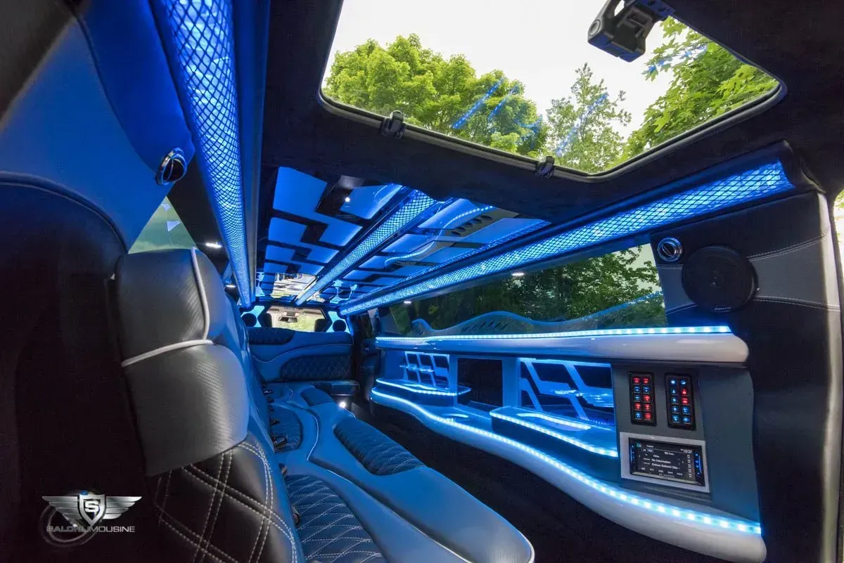 Interior view of a limousine with blue LED lighting and a sunroof, showing seating and bar area.