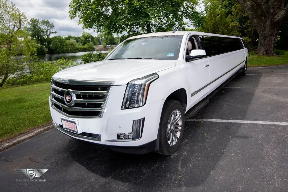 White Cadillac Escalade limousine parked on asphalt near greenery and a body of water.