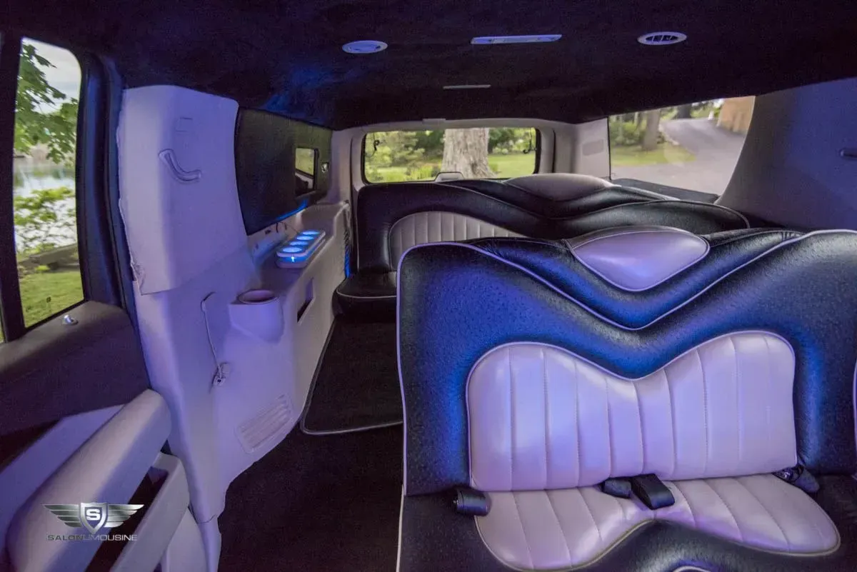 Interior of a limousine with black and light purple leather seating and a black ceiling with blue lighting.