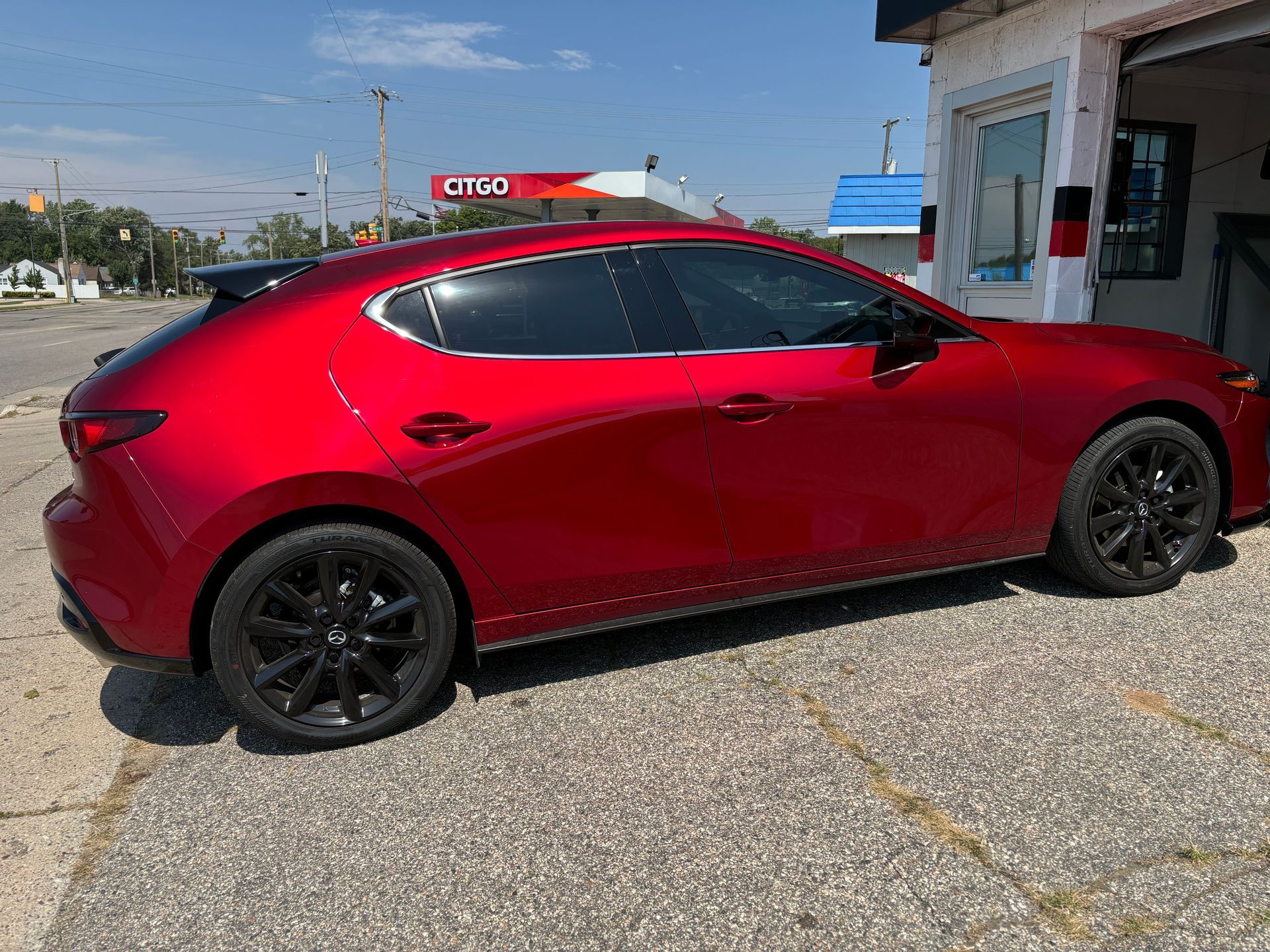 A red mazda 3 hatchback is parked in front of a gas station.
