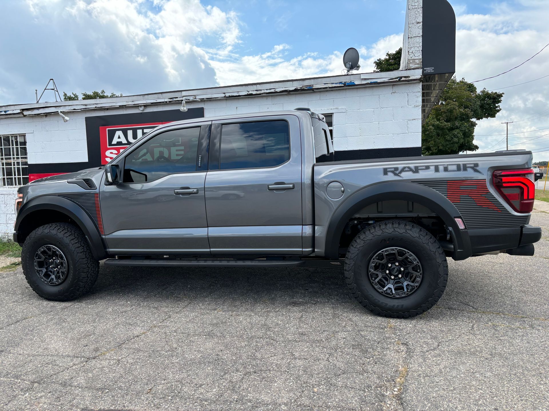 A gray ford raptor truck is parked in front of a white building.