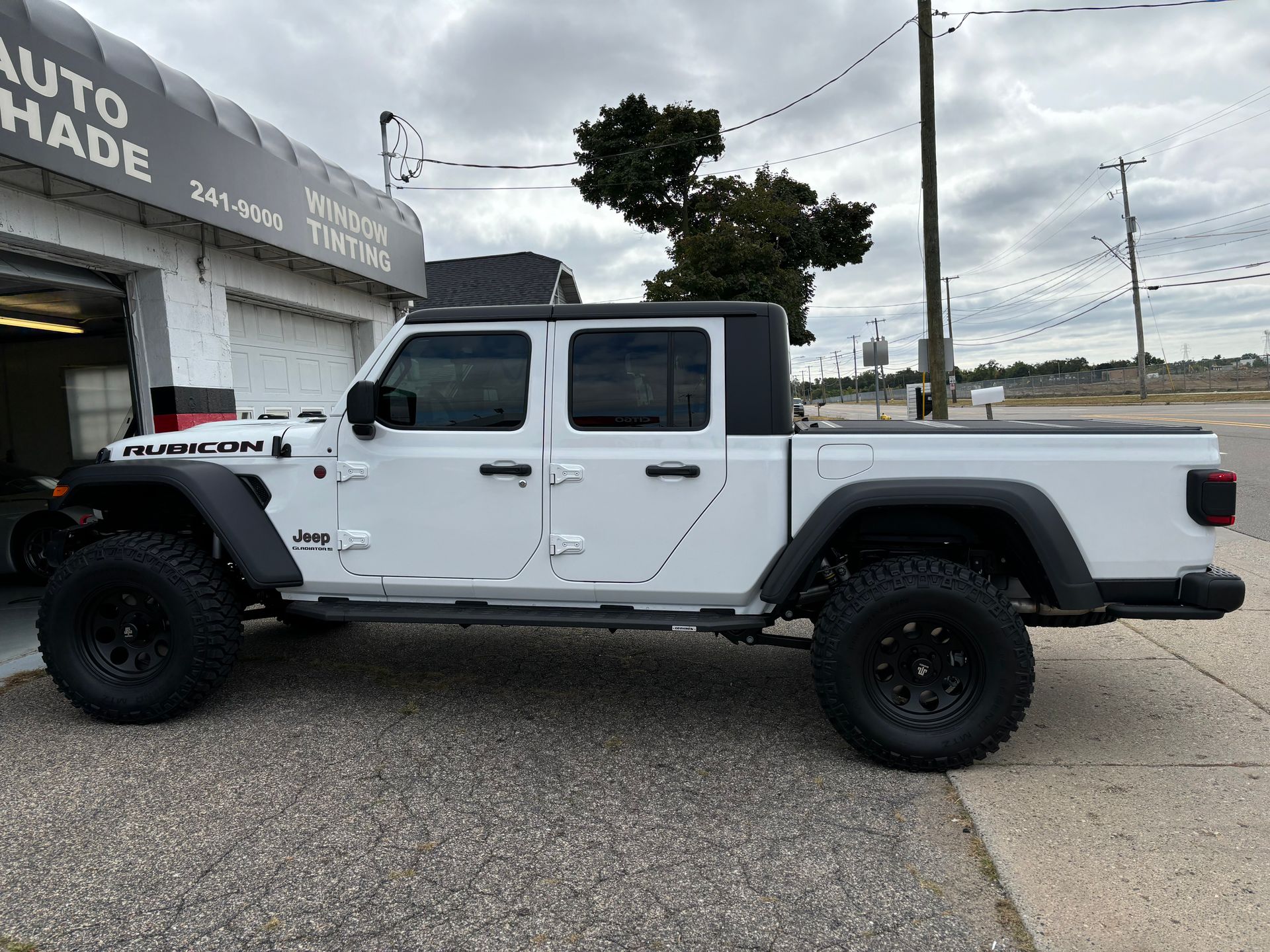A white jeep gladiator pickup truck is parked in front of a garage.