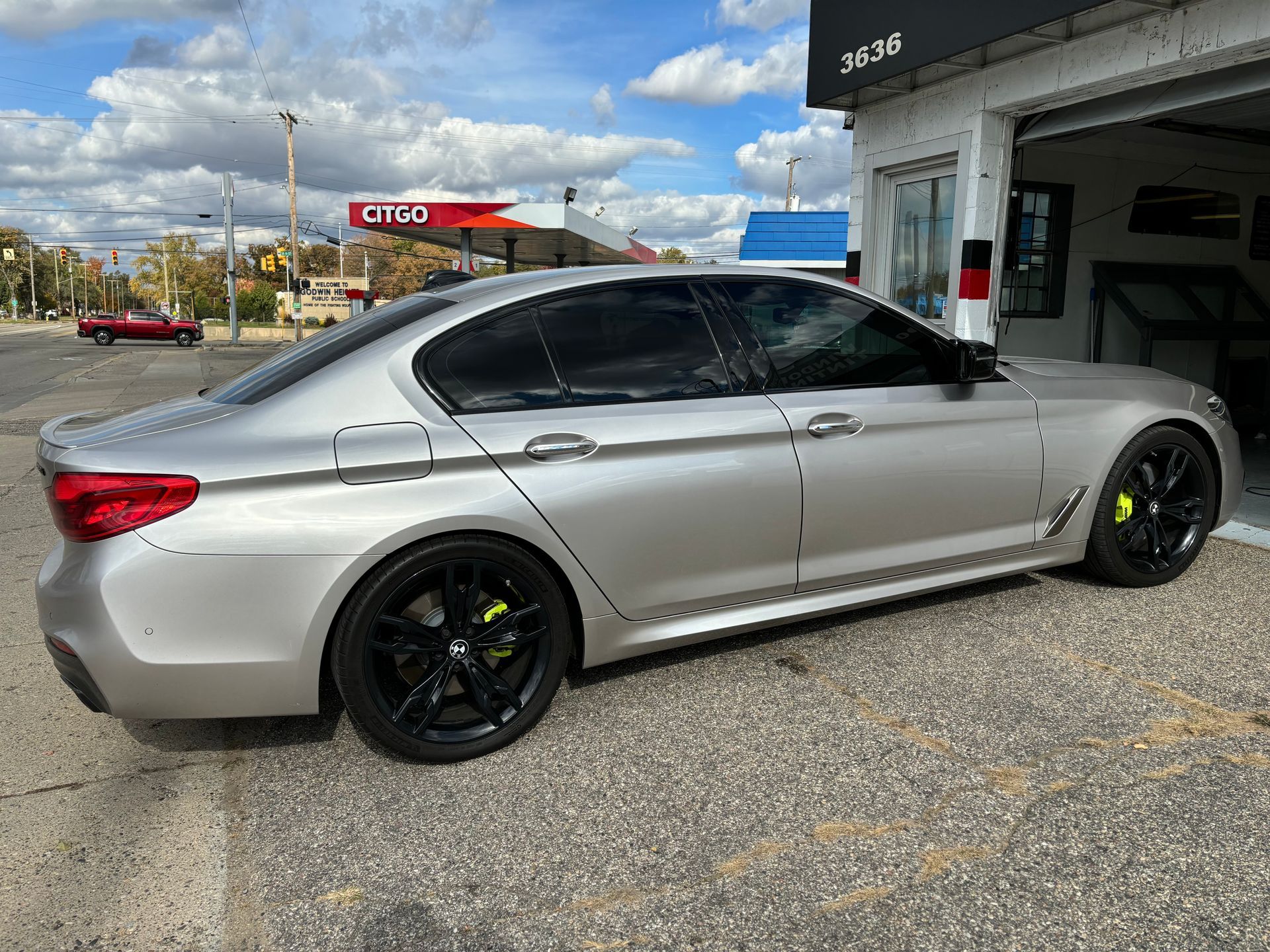 A silver bmw is parked in front of a gas station.