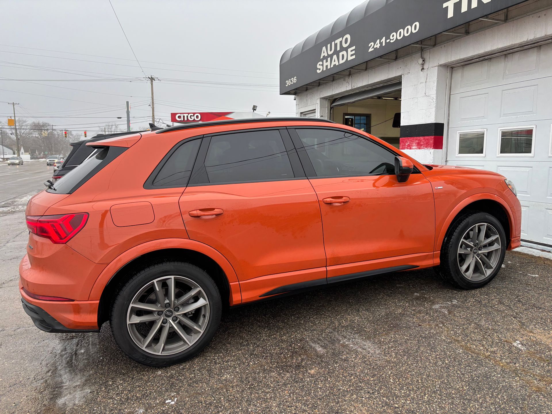 An orange audi q3 is parked in front of a garage.