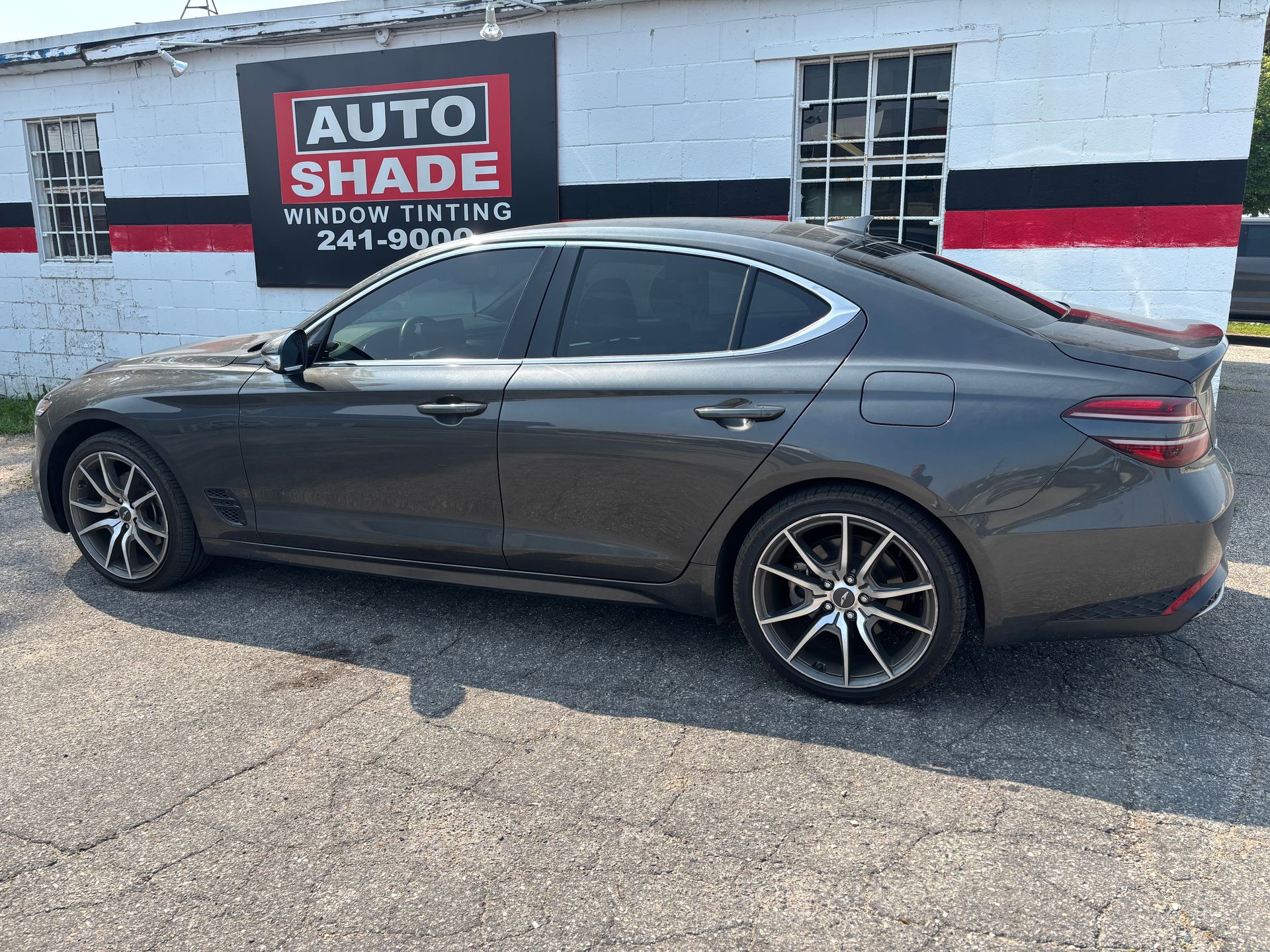 A gray car is parked in front of a building that says auto shade.