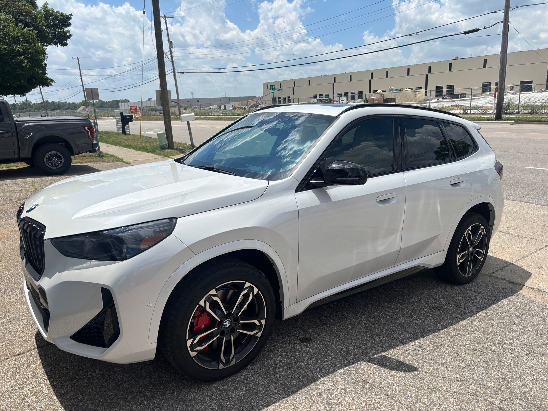 A white car is parked on the side of the road next to a truck.