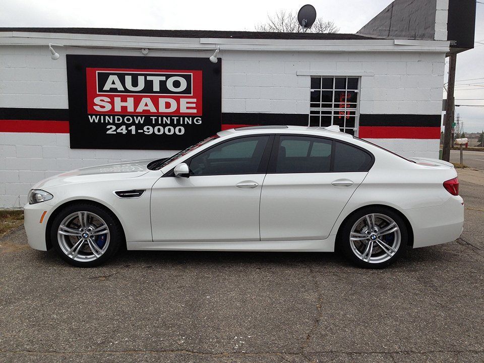 A white car is parked in front of a building that says auto shade window tinting.
