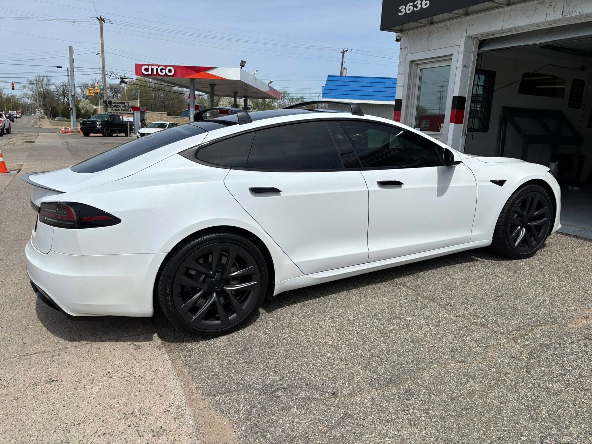 A white tesla model s is parked in front of a gas station.
