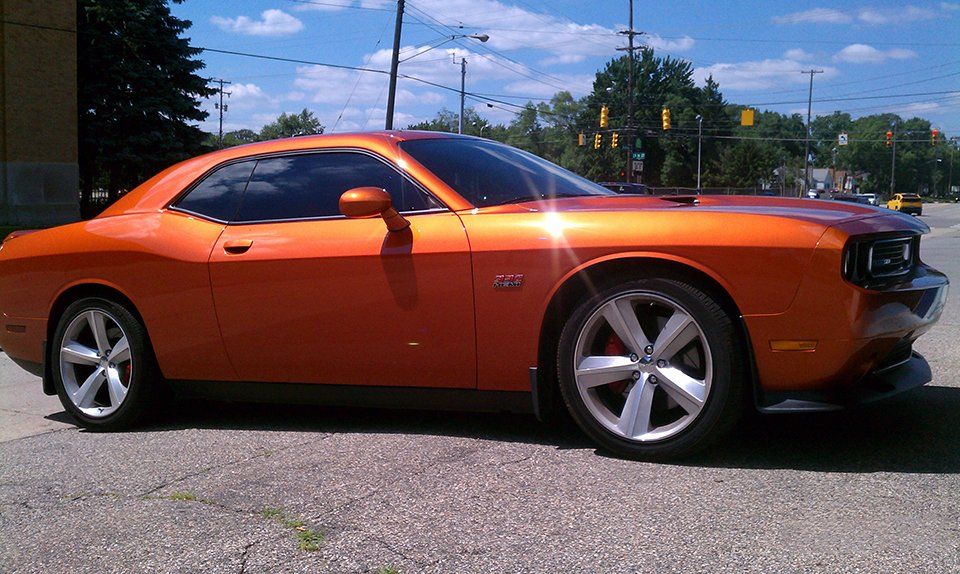 An orange dodge challenger is parked on the side of the road
