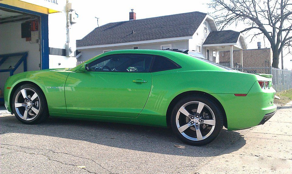 A green car is parked in front of a garage