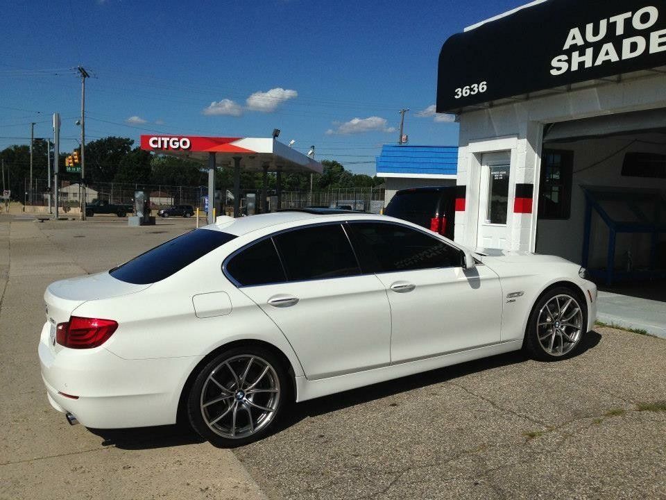A white car is parked in front of an auto shade shop