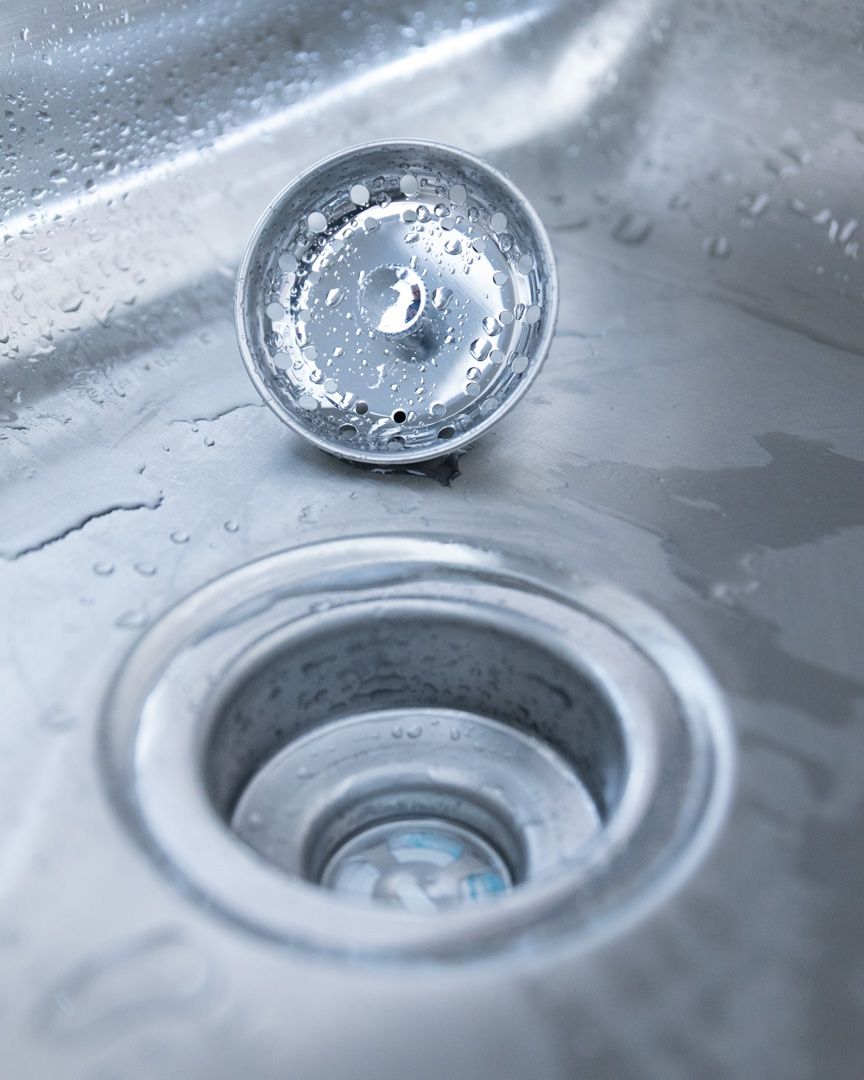 A metal sink drain with its matching strainer basket resting nearby on the basin surface.